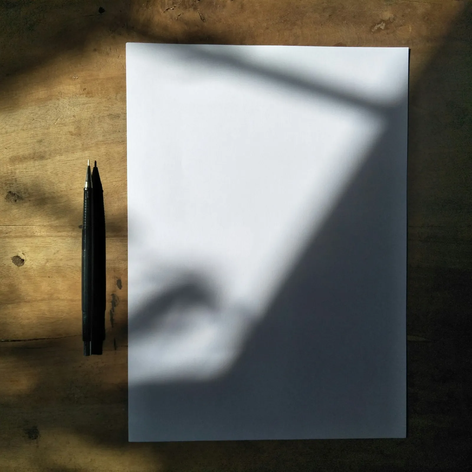 Feuille blanche et stylos posés sur un bureau en bois